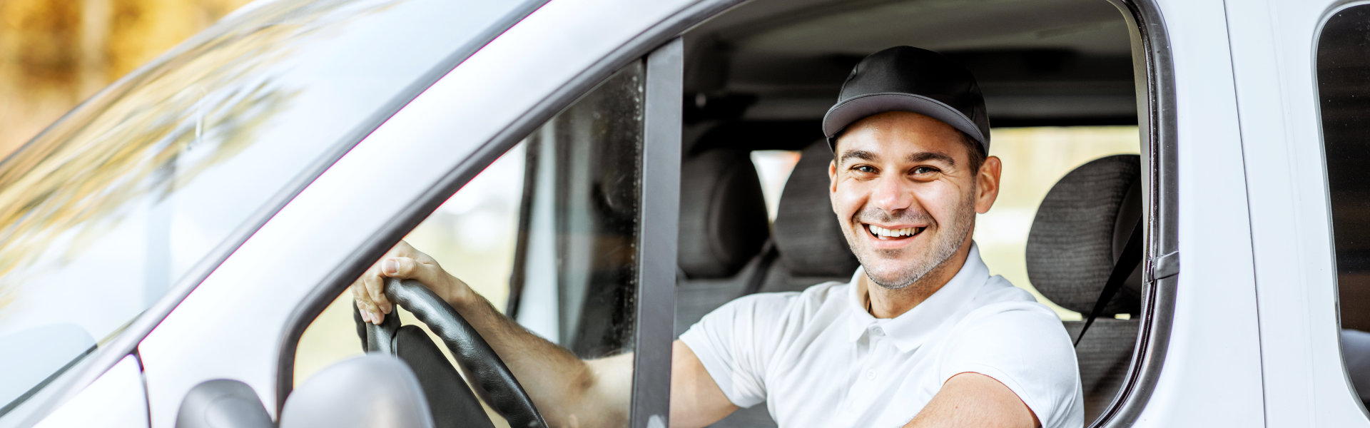 cheerful delivery driver in uniform looking out the window of the white cargo van vahicle