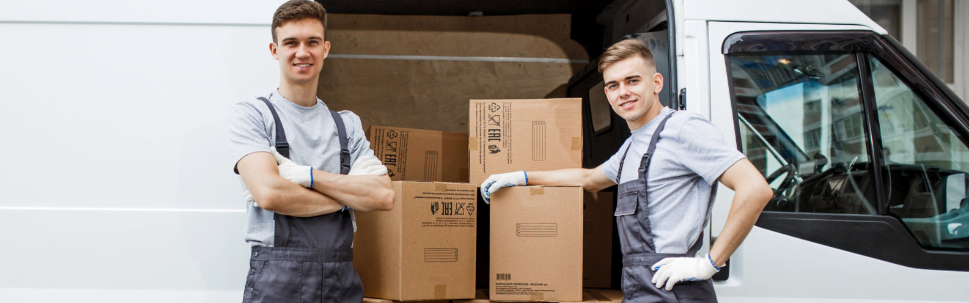 Two young handsome smiling workers wearing uniforms are standing next to the van full of boxes