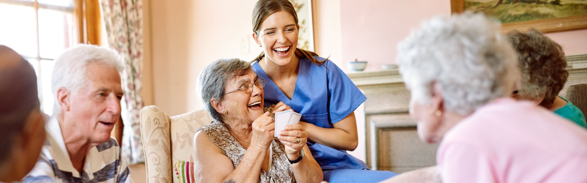 Shot of a group of happy seniors playing a card game in their retirement home while a nurse watches