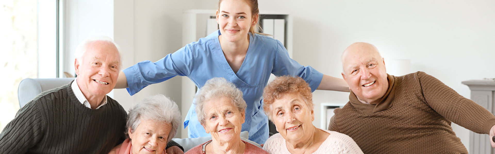 Young caregiver with group of senior people in nursing home